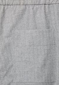 Tissu en chevrons gris avec une poche plaquée visible. Texture lisse, motif régulier et taille élastique.