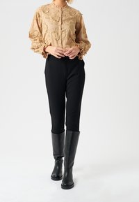 Light beige embroidered blouse with ruffled cuffs, paired with fitted black pants and knee-high black leather boots.