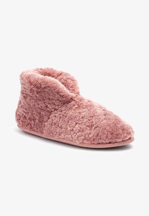 Chausson rose duveteux montant à la cheville, avec une surface extérieure douce et texturée et une semelle plate conçue pour une utilisation en intérieur.
