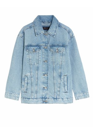 Personne portant une veste en denim bleu clair par-dessus une chemise blanche à boutons et un pantalon noir, debout avec les bras détendus le long du corps.