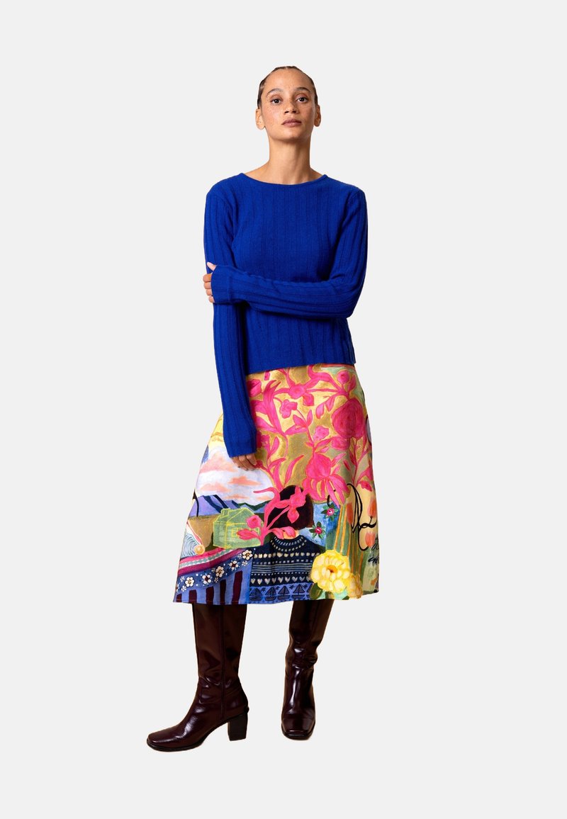 Blauwe geribde trui gecombineerd met een kleurrijke, lange rok met bloemrijke en abstracte patronen. Bruine laarzen tot aan de knie maken de look compleet.