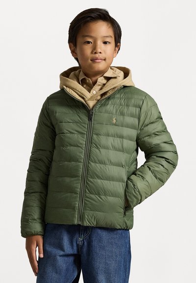 Green puffer jacket with a zip front, quilted design, and a beige hooded sweatshirt underneath. Worn with blue denim jeans.