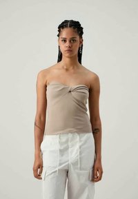 Beżowy, prążkowany top bez ramiączek z węzłem z przodu, zestawiony z białymi spodniami typu tapered. Minimalistyczny styl z gładką teksturą.