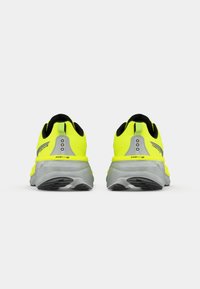 Paar neongelbe Laufschuhe mit grauen Sohlen von hinten auf einem schlichten weißen Hintergrund gesehen.