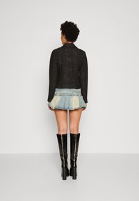 Czarna teksturowana krótka kurtka z kołnierzem, zestawiona z jasnoniebieską mini spódnicą dżinsową z falbaną u dołu. Czarne dopasowane kozaki za kolano.