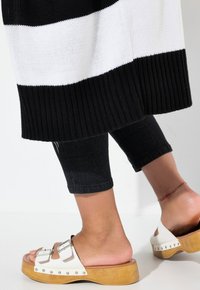 Suéter de punto con rayas en blanco y negro, dobladillo acanalado, combinado con jeans negros ajustados y sandalias de plataforma con doble hebilla.