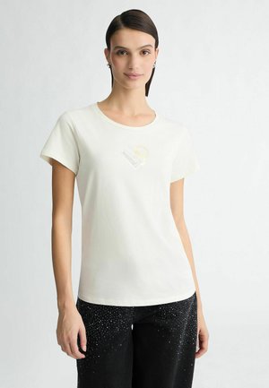 Crème kleurige katoenen t-shirt met een ronde hals en korte mouwen. Heeft een grafisch ontwerp op de borst, in combinatie met zwarte jeans versierd met strassstenen.