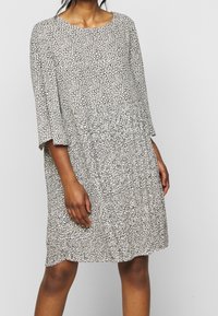 Mekko, jossa on mustavalkoinen kuviointi, pehmeä tuntuma, pyöreä pääntie ja kolmen neljänneksen kellohihat. A-linjainen muotoilu ja rento istuvuus.