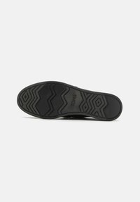 Black rubber shoe sole featuring a zigzag traction pattern and embossed "TOMS" logo. Smooth texture with a non-slip design.