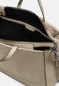 Beige Leder-Tote-Bag mit schwarzem Innenraum. Verfügt über einen Reißverschluss, mehrere Taschen und eine glatte Textur. Einfaches Design mit stabilen Griffen.
