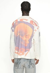 Beige Hemd mit langen Ärmeln, ausgestattet mit einem großen, bunten Totenschädel-Design, dem Text "NASA" und "1987", aus strukturiertem Stoff und mit lockerer Passform.
