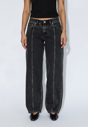 Czarne dżinsy z wysokim stanem i szerokimi nogawkami, z kontrastującymi przeszyciami, standardowymi kieszeniami oraz zapięciem na guziki. Tekstura jest miękka z delikatnym połyskiem.