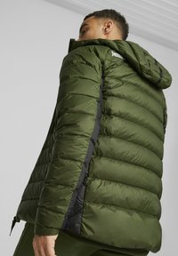 Puffjakke i olivengrøn med hætte, der har en quiltet design, lynlås lukning og sorte detaljer langs siderne.