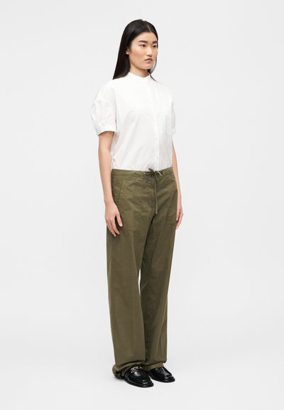 Λευκό πουκάμισο με κοντά μανίκια και κουμπιά, με φουσκωτά μανίκια, σε συνδυασμό με φαρδιά ελιάς πράσινα παντελόνια και μαύρα μοκασίνια.