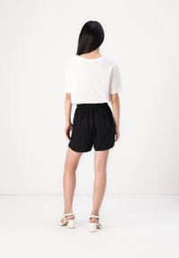 Svarta shorts med elastisk midja kombinerade med en vit t-shirt med kort ärm. Skorna är ljusa klackar med remmar.