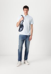 Light blue polo shirt with short sleeves and a zippered collar, paired with faded blue jeans and white sneakers. Black and blue sling bag.