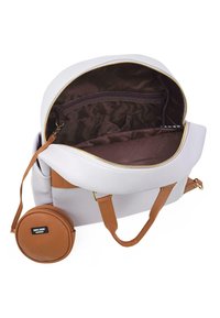 Mochila gris clara con parte superior con cremallera, correas marrones texturizadas y un bolsillo interior. Incluye un accesorio circular desmontable.