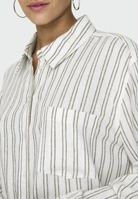 Camicia bianca con bottoni, realizzata in lino, con taschino, caratterizzata da sottili righe verdi verticali e un design di colletto classico.