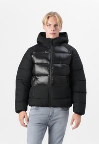 Doudoune noire avec une finition brillante, capuche, fermeture éclair, deux poches avant et design à panneaux. Fabriquée en matériau léger et isolé.