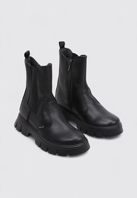 Bottines en cuir noir avec une semelle en caoutchouc épaisse, fermeture éclair sur le côté et panneaux élastiques pour un enfilage et un retrait faciles. Texture lisse, design minimaliste.