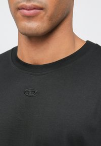 Μαύρη βαμβακερή μπλούζα τύπου crew-neck με υφασμένο λογότυπο πάνω από το στήθος. Λείο ύφασμα με κανονική εφαρμογή και ριμπέ λαιμό.