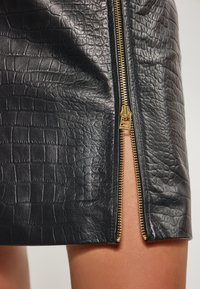 Sort faux læder mini skirt med krokodille tekstur og en guld lynlås detalje på siden. Glat overflade med skræddersyet pasform.