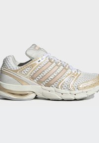 Hellbeiger und weißer Sportschuh mit Mesh-Obermaterial, Kunststoffüberzügen, gepolsterter Sohle und weißen Schnürsenkeln auf einfarbigem Hintergrund.