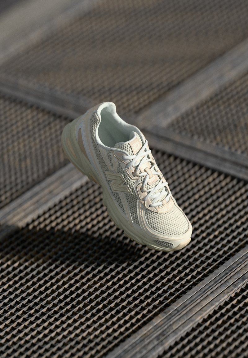 Scarpa da corsa beige chiaro con tomaia in rete, lacci leggeri e suola ammortizzata, mostrata su una superficie metallica texture.
