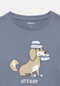 Blue shirt with cartoon dog wearing striped nightcap and slippers, holding a matching pillow, text reads "LET'S SLEEP."