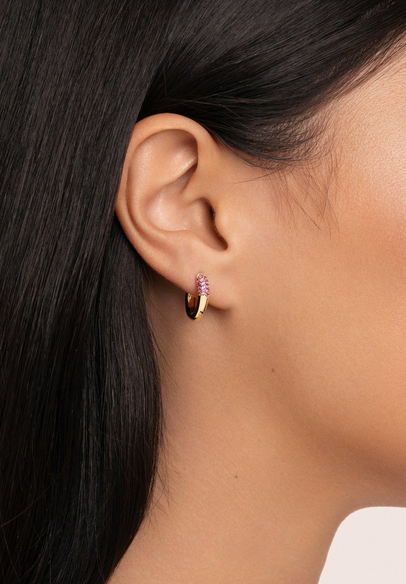 Boucle d'oreille en or avec un accent en pierre précieuse rose, présentant une surface lisse et brillante et un design arrondi, portée sur le lobe de l'oreille.