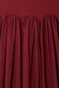 Jupe bordeaux avec un tissu froncé, présentant une taille en dentelle et une finition lisse et texturée. Le tissu tombe de manière lâche et élégante.
