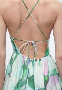 Οπίσθια όψη γυναίκας που φοράει φόρεμα με λουλουδάτο σχέδιο, λεπτές λουρίδες σε σταυρωτό στυλ και δεμένο φιόγκο στο κάτω μέρος της πλάτης.