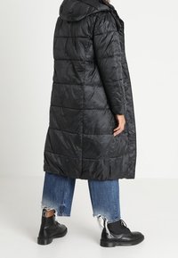 Černá péřová bunda s kapucí a prošívaným designem. Kombinovaná s krátkými džíny s potrhaným vzhledem a černými kotníkovými botami.