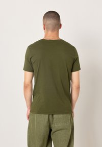 Olivno zelena majica z okroglim izrezom iz mehkega blaga s kratkimi rokavi, z enostavnim dizajnom in sproščenim krojem. Primerna za vsakodnevno nošenje.