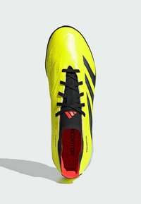 Chaussure de football jaune vif avec une surface texturée, des accents noirs et un intérieur rouge. Présente des lacets noirs contrastants et des détails de marque.