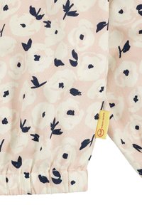 Helle rosa Stoff mit floralem Muster, das marineblaue Blumen und Blätter zeigt. Enthält ein gelbes Etikett mit Branding und eine geraffte Manschettendetail.
