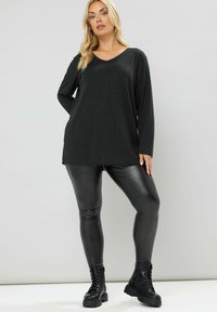 Maglietta nera a maniche lunghe con scollo a V e un sottile motivo di paillettes, abbinata a leggings neri lucidi e stivali militari con lacci.