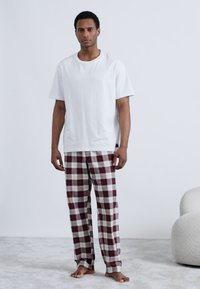 Weißes T-Shirt mit kurzen Ärmeln, kombiniert mit rot-weiß karierten Pyjamahosen, ausgestattet mit lockerem Schnitt und glattem Baumwollstoff.