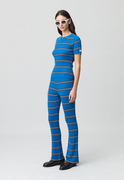 Completo due pezzi a righe blu con top aderente a maniche corte e pantaloni svasati, realizzato in un materiale morbido al tatto. Occhiali da sole bianchi.