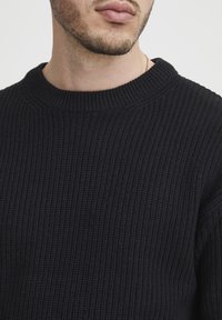 Dark navy knitted sweater with a ribbed texture, crew neckline, and slightly oversized fit. No visible embellishments or patterns.