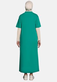 Mekko pitkä teal-väri, jossa on lyhyet hihat, löysä malli ja suora leikkaus. Päällä vaalean värinen pitkähihaisen paidan ja valkoisten tennareiden kanssa.