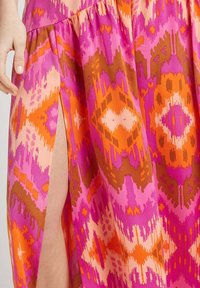 Robe maxi avec des motifs géométriques vibrants en rose, orange et marron, dotée d'une fente sur le côté et d'une texture de tissu douce.