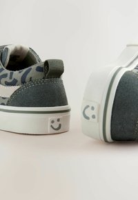 Zamszowe sneakersy w zielonym kamuflażu z białą gumową podeszwą, z uśmiechniętą buźką na pięcie.