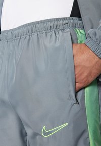 Nike Sporthose in Grau, mit einem dezenten Glanz, elastischem Bund, grünen Seitenakzenten und einem kleinen, gestickten Logo in Neon-Gelb.