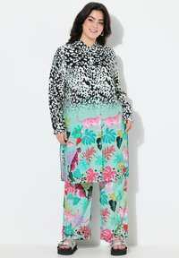 La camicia a maniche lunghe presenta un motivo animalier in bianco e nero, abbinata a pantaloni larghi verde menta decorati con colorati motivi tropicali.
