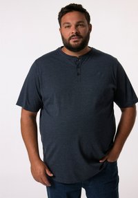 Camisa henley de manga corta azul marino con tres botones negros en el cuello, hecha de un tejido suave, combinada con jeans azules.