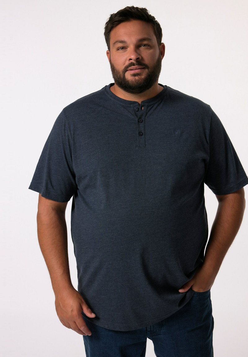 Camisa henley de manga corta azul marino con tres botones negros en el cuello, hecha de un tejido suave, combinada con jeans azules.