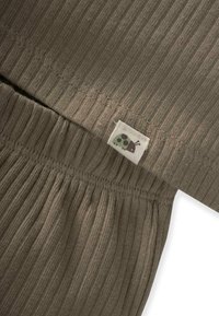 Khaki ribbad tyg med rynkad elastisk midjeband. Har en liten tyglabel med en flerfärgad nyckelpiga-design.