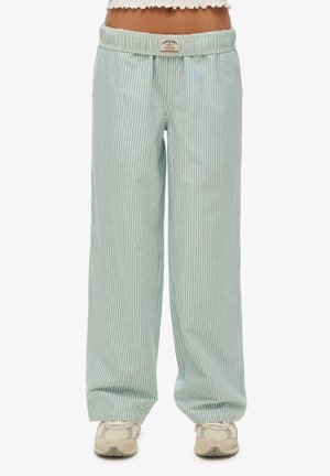 Pantalones sueltos de rayas verticales en verde claro y blanco con cintura elástica y zapatillas deportivas en una persona de pie.