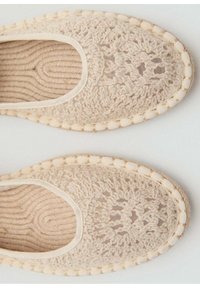 Zapatillas de ganchillo beige con un patrón texturizado, abertura elástica y punta redondeada. Acentuadas con un borde tejido alrededor de la suela.